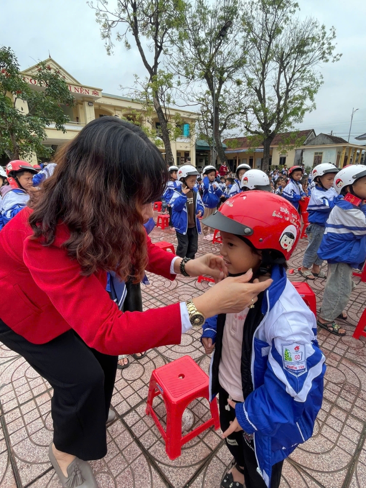 Cô Tổng đang cài mũ bảo hiểm cho các con